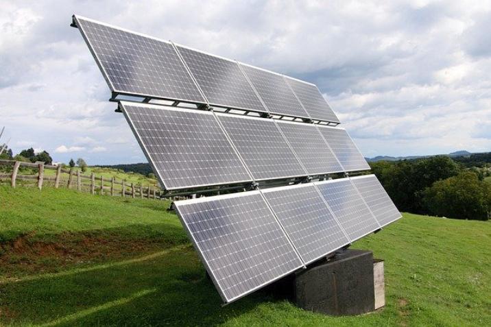 CONJUNTO DE PAINÉIS SOLARES INSTALADOS EM UM CAMPO VERDE, COM UMA CERCA AO FUNDO E UM CÉU PARCIALMENTE NUBLADO