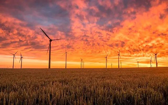 TORRES DE ENERGIA EÓLICA EM UMA GRANDE ÁREA ABERTA E NO FUNDO O PÔR DO SOL