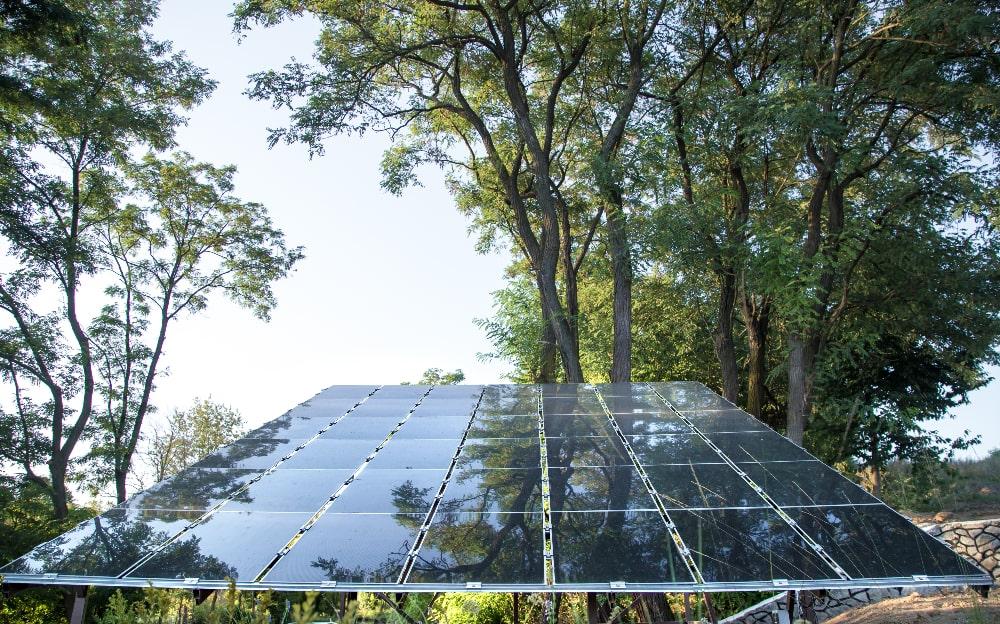 INSTALAÇÃO DE UM SISTEMA DE ENERGIA SOLAR FOTOVOLTAICA E AO FUNDO ALGUMAS ÁRVORES