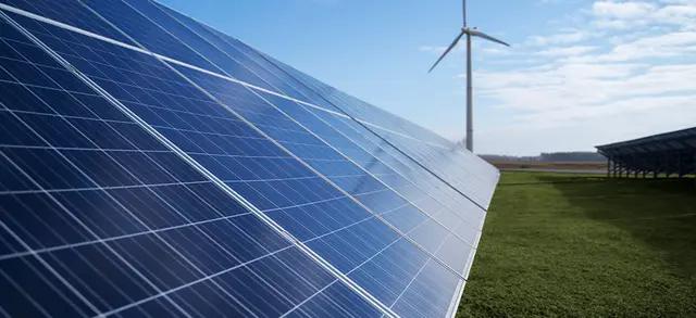 PLACAS DE ENERGIA SOLAR E UMA TORRE DE ENERGIA EÓLICA AO FUNDO