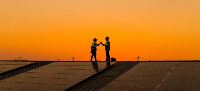DUAS PESSOAS AO FUNDO E NO LADO DE VÁRIAS PLACAS DE ENERGIA SOLAR FOTOVOLTAICA