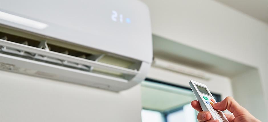 PESSOA COM UM CONTROLE NA MÃO LIGANDO O APARELHO DE AR CONDICIONADO ALIMENTADO COM PLACAS DE ENERGIA SOLAR