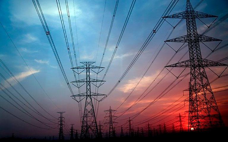 VÁRIAS TORRES DE ENERGIA ELÉTRICA COM MUITOS CABOS CONECTADOS A ELA E UM CÉU COLORIDO AO FUNDO