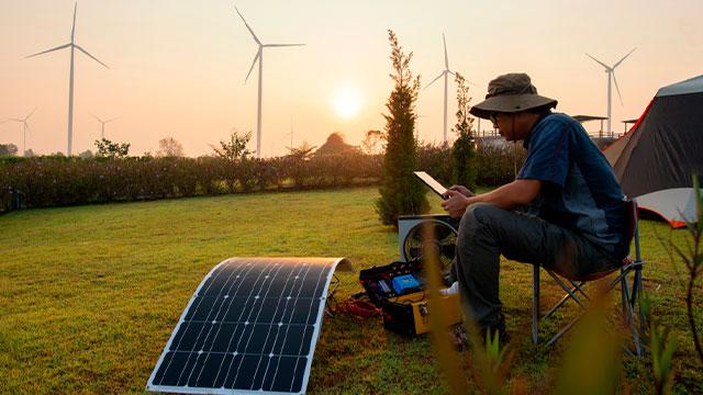 PESSOA SENTADA MEXENDO EM SEU CELULAR E USANDO UM GERADOR DE ENERGIA SOLAR PORTÁTIL