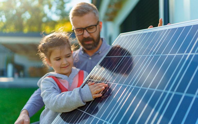 PAI E FILHA AO LADO DE UMA PLACA SOLAR FOTOVOLTAICA