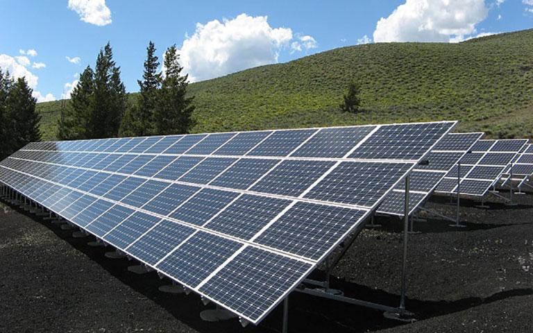 GRANDE QUANTIDADE DE PLACAS DE ENERGIA FOTOVOLTAICAS EM UMA ÁREA ABERTA E AO FUNDO MONTANHAS